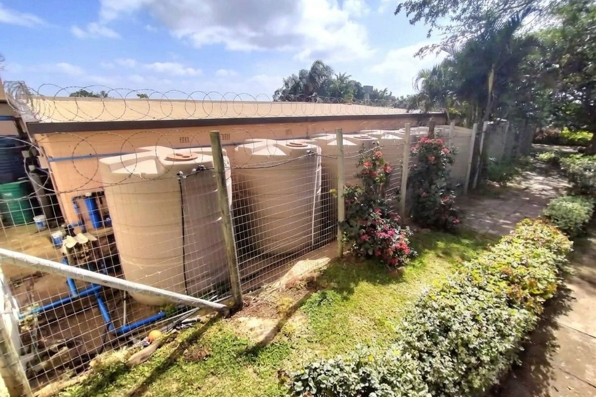 Rear exterior area featuring multiple water storage tanks secured behind mesh fencing with razor wire topping.