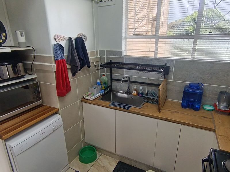 Compact kitchen featuring a stainless steel sink, wooden countertops, tiled backsplash, and built-in cabinetry with a window providing natural light.