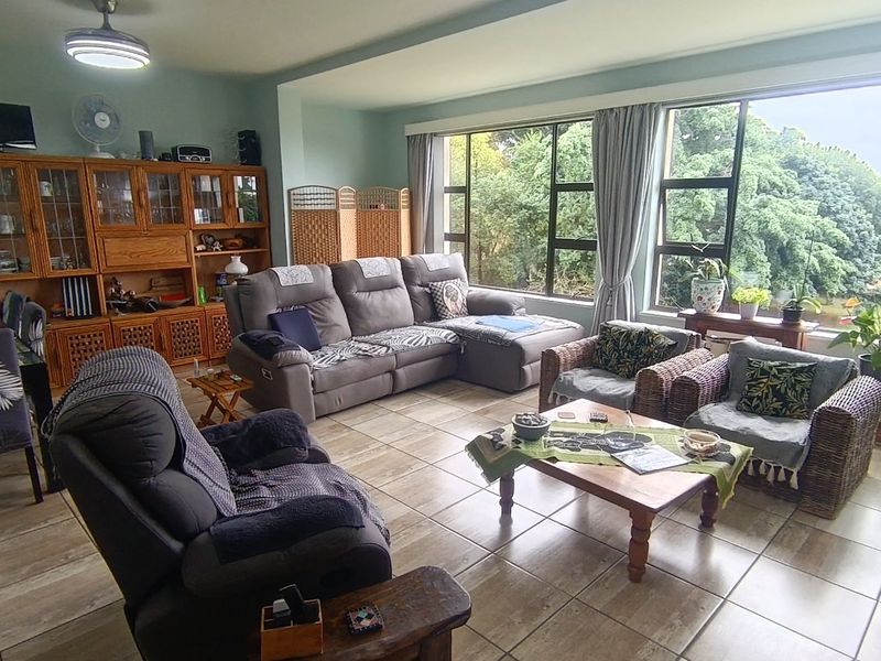 Spacious living area featuring large windows with garden views, tiled flooring, and a ceiling fan, offering a bright and comfortable space.