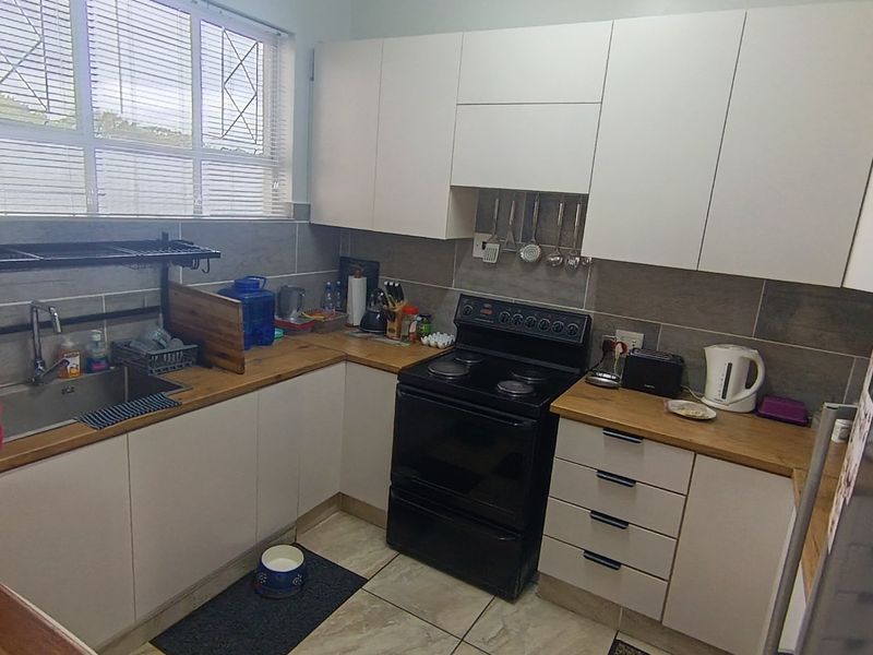 A functional kitchen featuring white cabinetry, wooden countertops, a tiled backsplash, and a freestanding electric stove, complemented by tiled flooring and natural light.