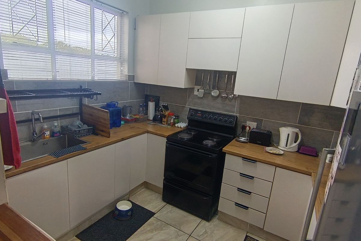 A functional kitchen featuring white cabinetry, wooden countertops, a tiled backsplash, and a freestanding electric stove, complemented by tiled flooring and natural light.