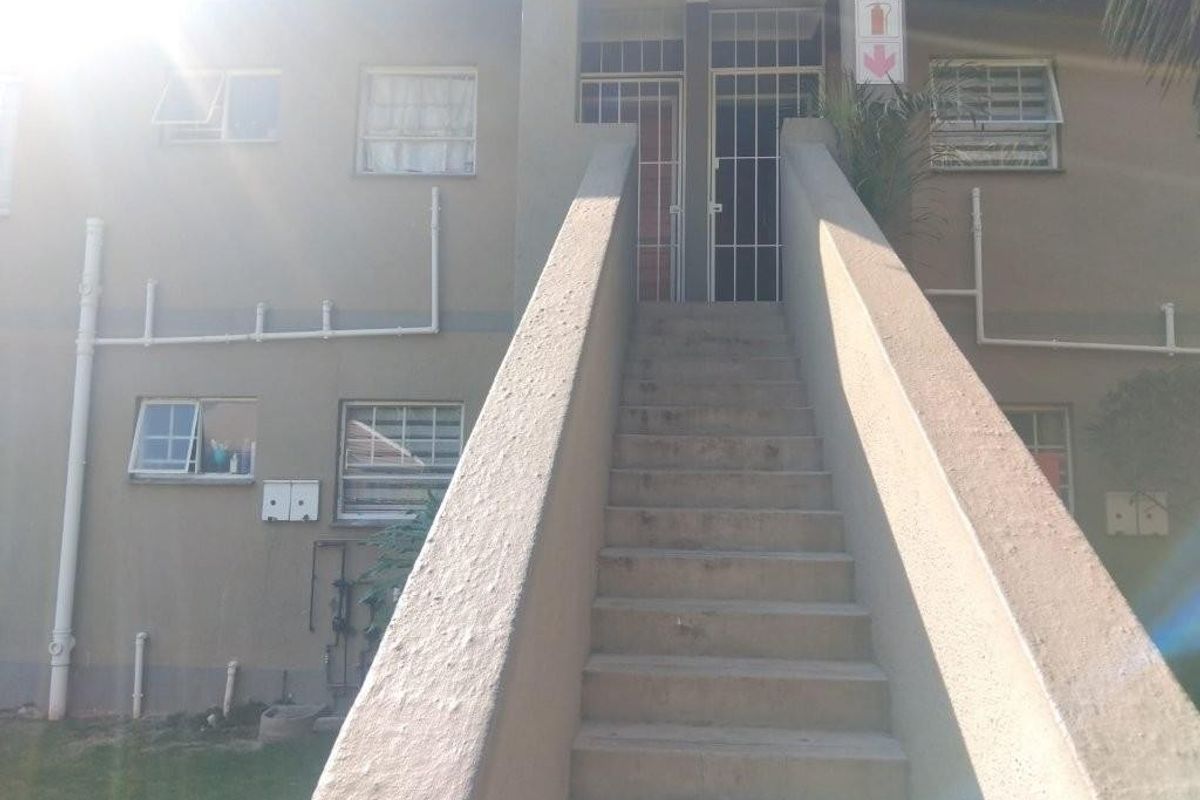 Exterior view of an apartment building featuring a central concrete staircase leading to upper-level entrances with security gates and casement windows.