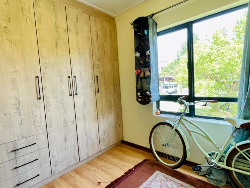 A bedroom featuring light wood-look built-in cupboards, laminate flooring, and a large window providing natural light.