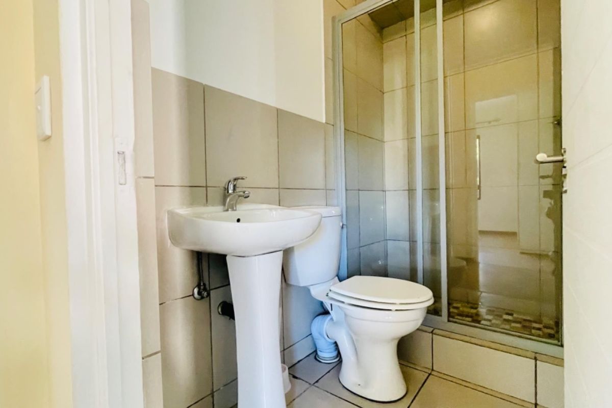A functional bathroom featuring a pedestal basin, toilet, and a glass-enclosed shower with neutral wall and floor tiling.