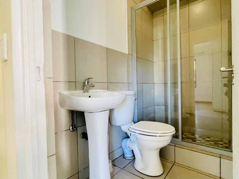 A functional bathroom featuring a pedestal basin, toilet, and a glass-enclosed shower with neutral wall and floor tiling.