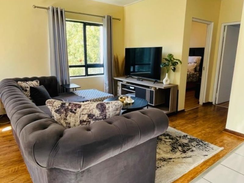 A living room featuring a mix of laminate and tiled flooring, with a window providing natural light and access to adjacent rooms.