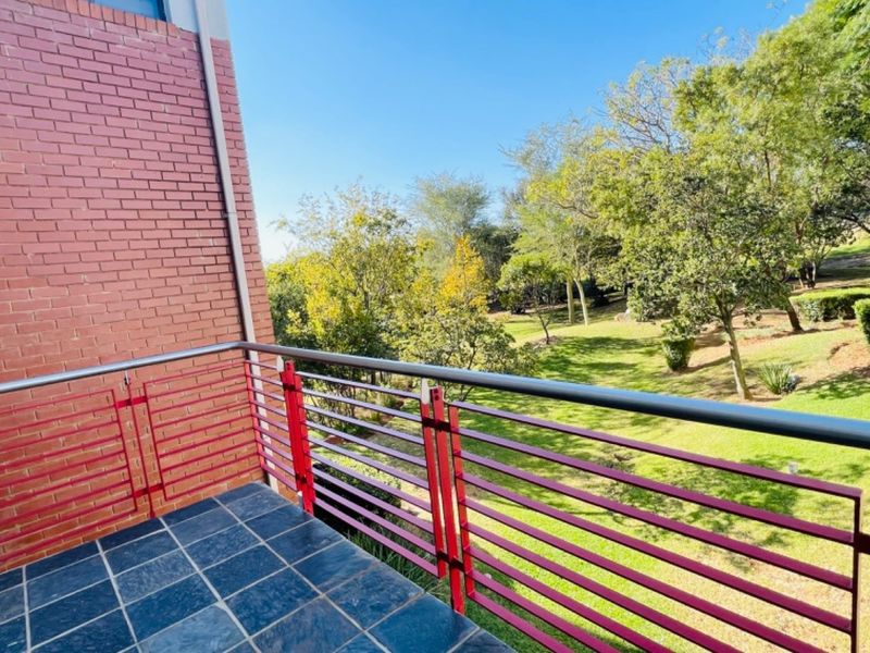 A private balcony featuring tiled flooring and a red metal balustrade, overlooking a lush green garden area.
