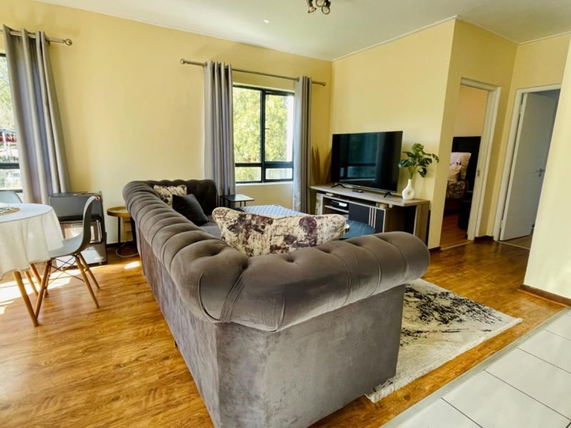A bright living room featuring laminate flooring, neutral walls, and large windows that provide natural light, creating a comfortable and inviting living space.