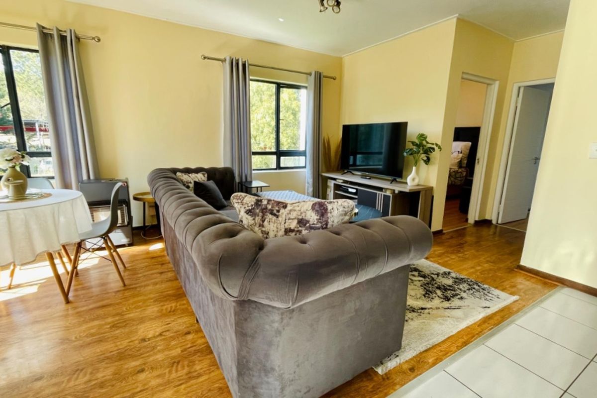A bright living room featuring laminate flooring, neutral walls, and large windows that provide natural light, creating a comfortable and inviting living space.