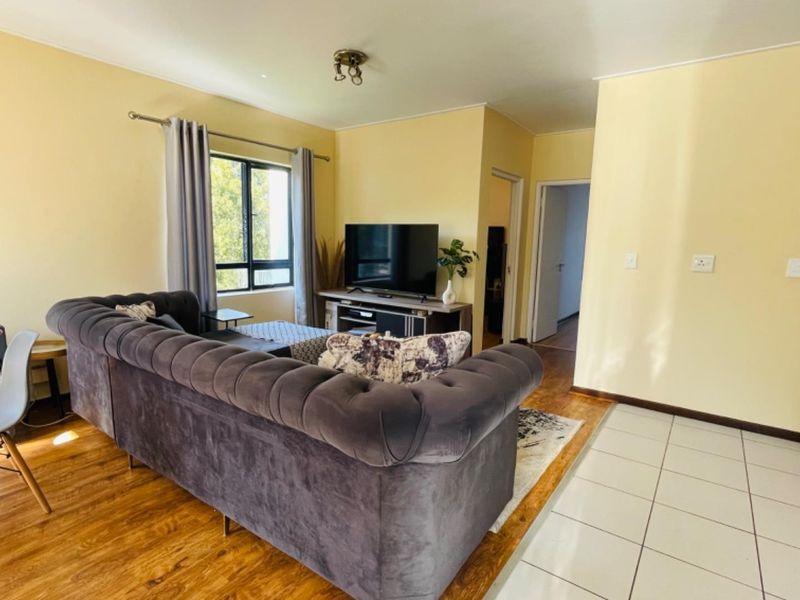 A living room featuring a combination of laminate and tiled flooring, neutral wall tones, and natural light from the window.