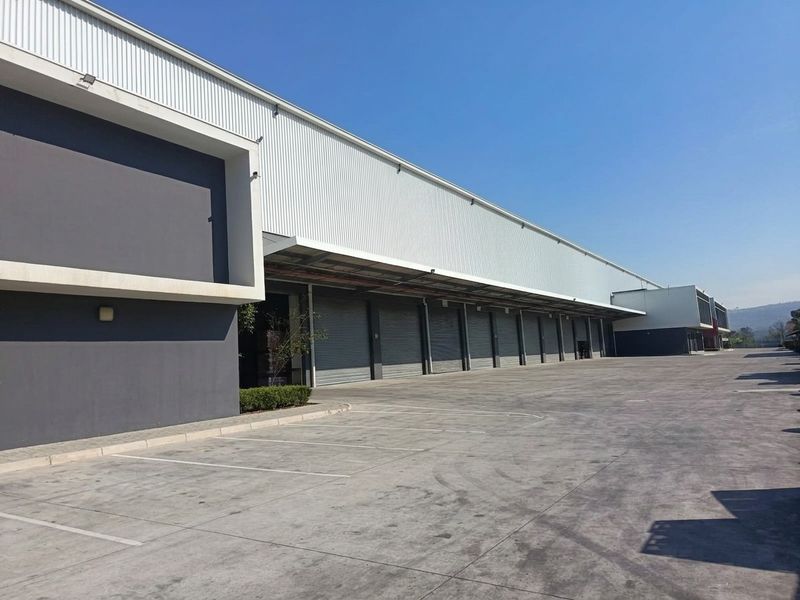 Industrial warehouse facility featuring multiple roller shutter doors, a large concrete hardstand area, and modern corrugated metal cladding.
