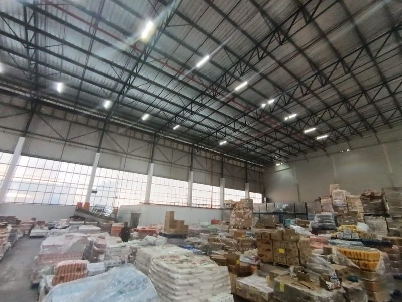 Spacious industrial warehouse featuring high ceilings with exposed steel trusses, large windows for natural light, and functional overhead lighting.