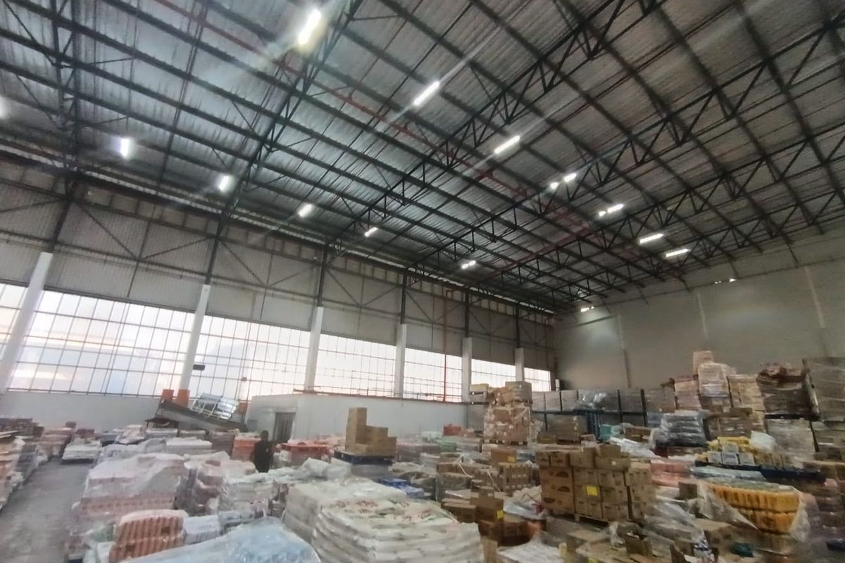 Spacious industrial warehouse featuring high ceilings with exposed steel trusses, large windows for natural light, and functional overhead lighting.