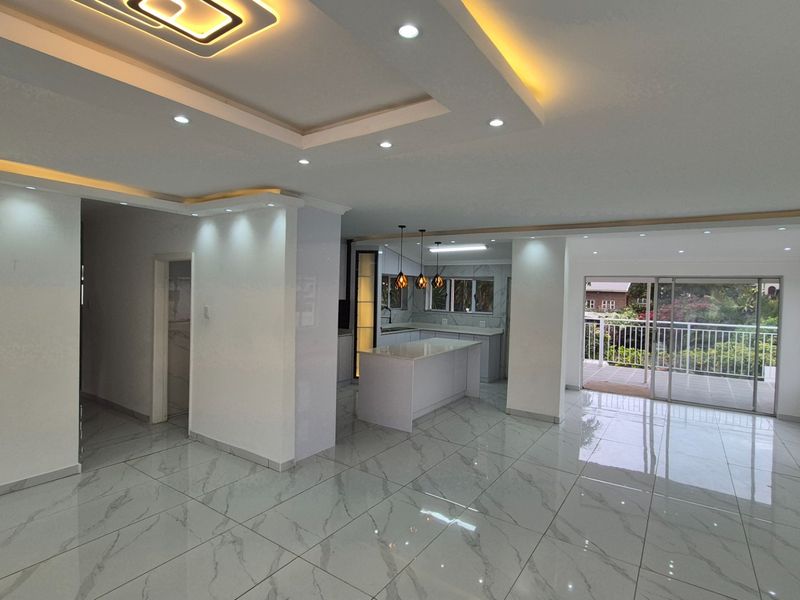 Spacious open-plan living and kitchen area featuring modern coffered ceilings, recessed lighting, and polished marble-look floor tiles with direct access to a balcony.
