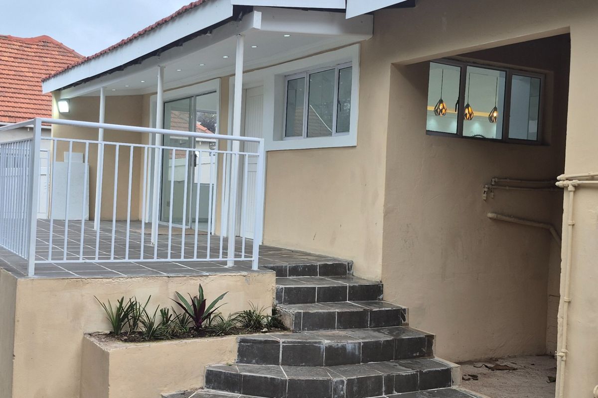 Rear exterior view featuring a tiled patio with metal balustrade, recessed lighting, and direct access via sliding glass doors.