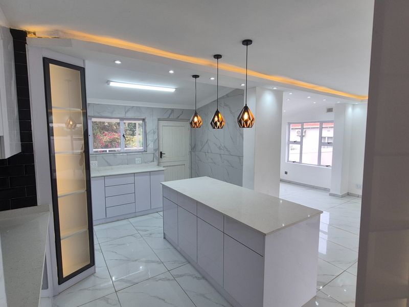 Modern open-plan kitchen featuring a central island, sleek white cabinetry, marble-look floor tiles, and contemporary pendant lighting in a bright, spacious layout.