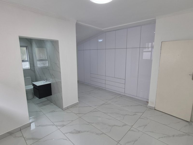 Modern bedroom featuring large built-in cupboards, polished porcelain floor tiles, and an integrated en-suite bathroom with a contemporary vanity.