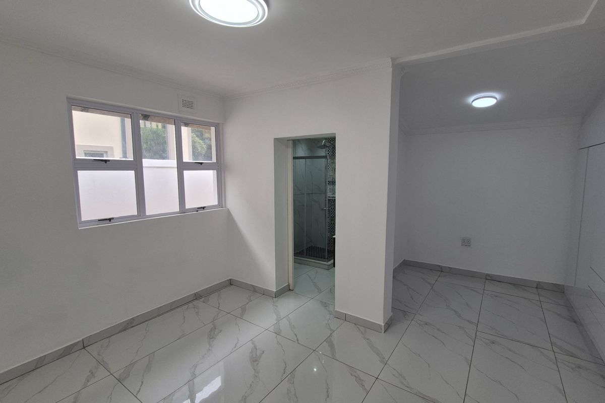 A bright, empty bedroom featuring modern marble-look tiled flooring, built-in cupboards, and an attached en-suite bathroom.
