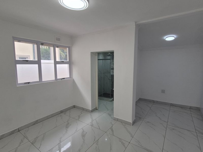 A bright, empty bedroom featuring modern marble-look tiled flooring, built-in cupboards, and an attached en-suite bathroom.