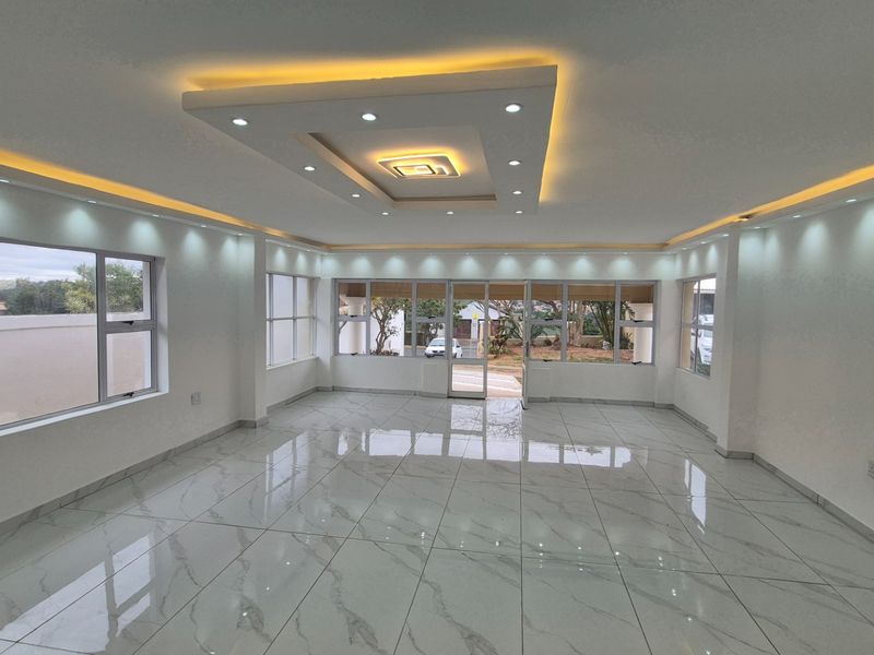 Spacious, bright living area featuring modern recessed ceiling lighting, large format marble-look floor tiles, and extensive aluminium-framed windows and doors.