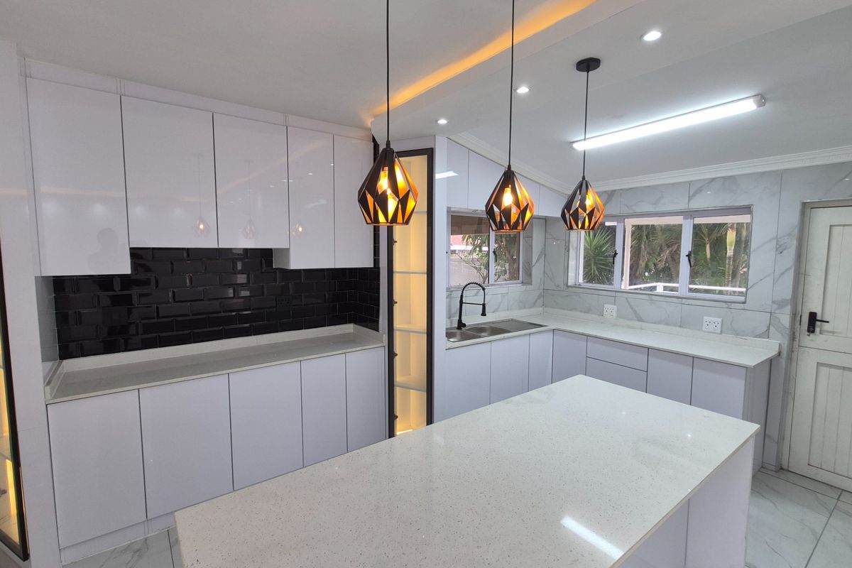 A modern, renovated kitchen featuring white cabinetry, quartz countertops, a central island, and stylish black subway tile backsplash with contemporary pendant lighting.