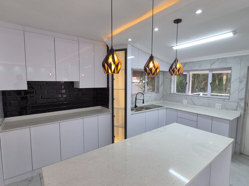 A modern, renovated kitchen featuring white cabinetry, quartz countertops, a central island, and stylish black subway tile backsplash with contemporary pendant lighting.