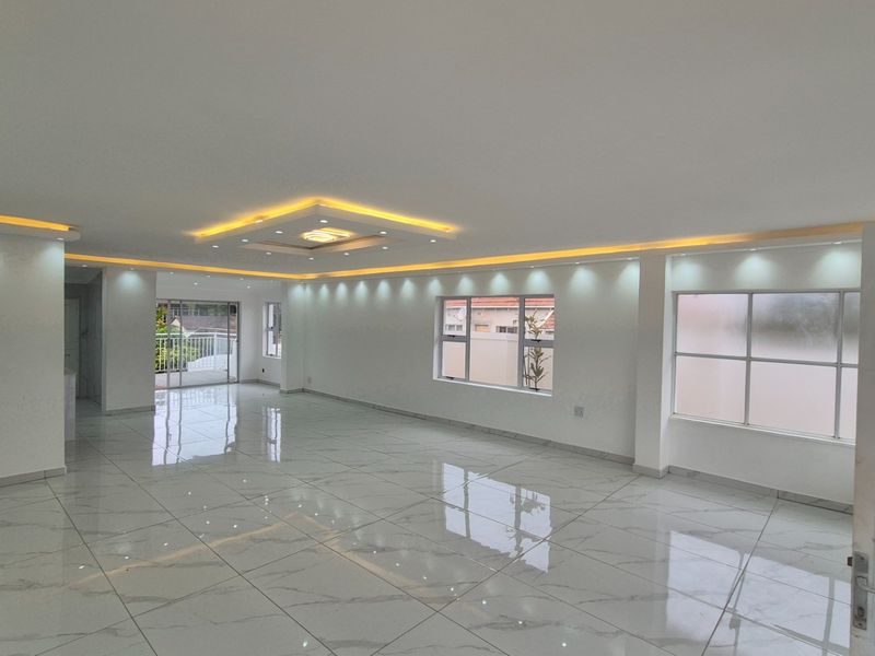 Spacious open-plan living area featuring modern recessed ceiling lighting, cove lighting, and high-gloss porcelain floor tiles throughout.