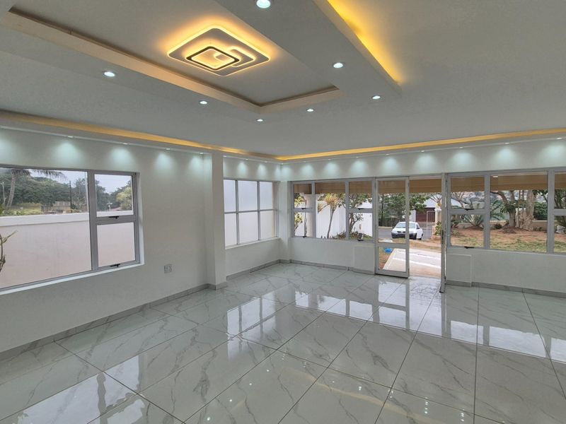 Spacious, light-filled living area featuring modern recessed ceiling lighting, cove lighting, and polished porcelain floor tiles with large aluminium windows and doors.