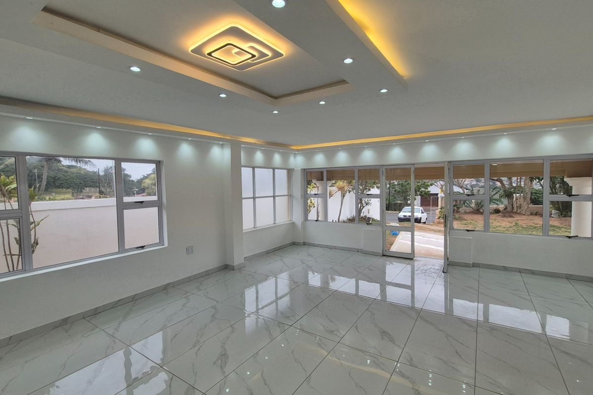 Spacious, light-filled living area featuring modern recessed ceiling lighting, cove lighting, and polished porcelain floor tiles with large aluminium windows and doors.