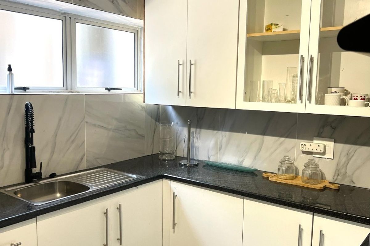 A well-maintained kitchen featuring white cabinetry, granite countertops, marble-look splashbacks, and a modern gooseneck faucet.