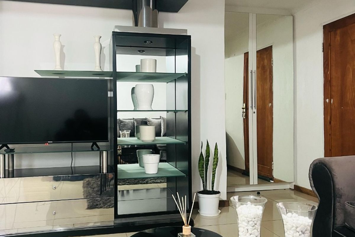 A modern living room featuring a built-in media console, tiled flooring, and mirrored closet doors, creating a bright and functional living space.