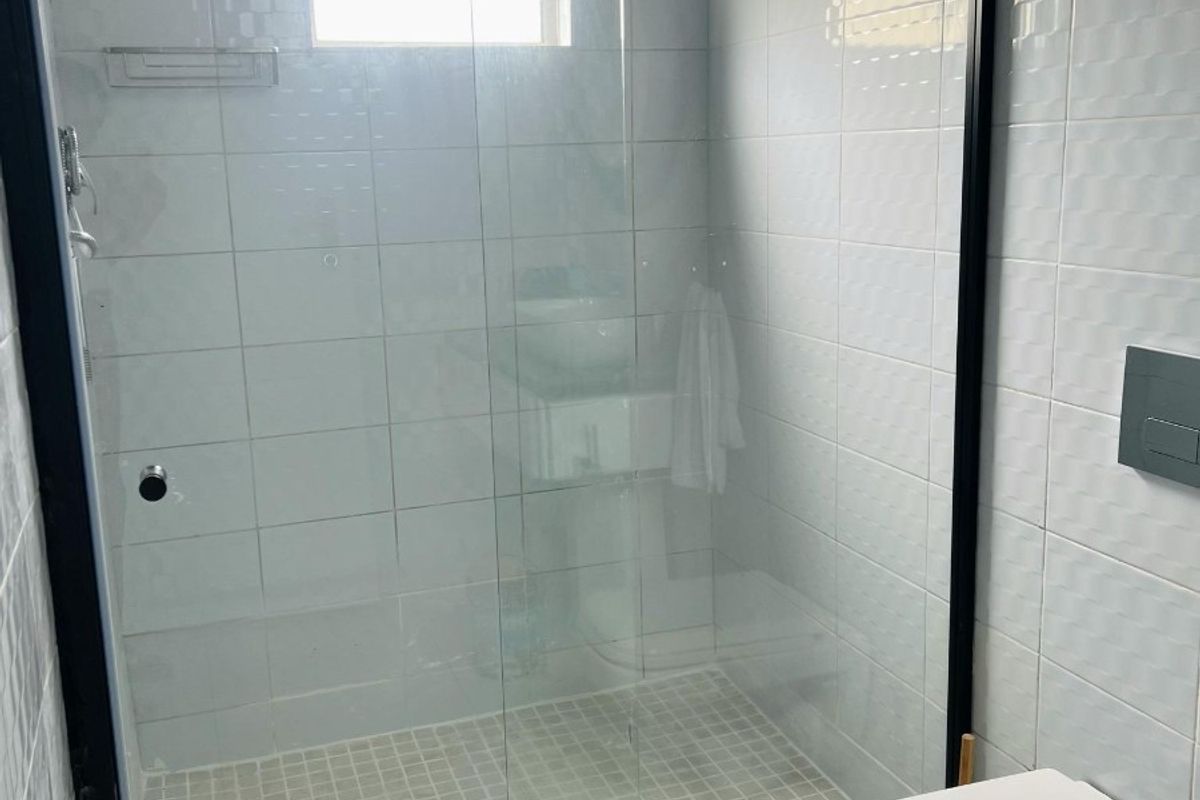 A modern bathroom featuring a walk-in shower with a black-framed glass screen, wall-mounted toilet, and clean white tiled finishes.