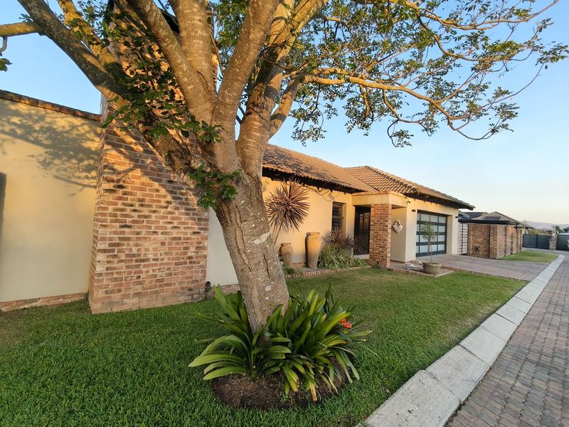 Front elevation of a well-maintained single-story house featuring a brick chimney, tiled roof, and a paved driveway leading to a modern garage.