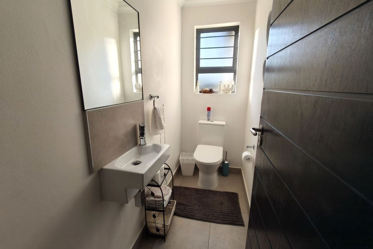 A clean and modern guest bathroom featuring a wall-mounted basin, toilet, and neutral tiled flooring with natural light from a window.