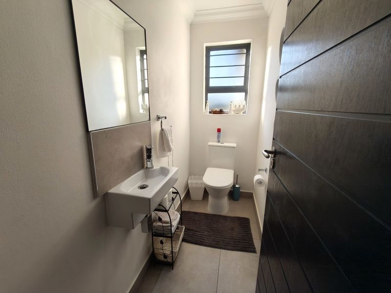 A clean and modern guest bathroom featuring a wall-mounted basin, toilet, and neutral tiled flooring with natural light from a window.
