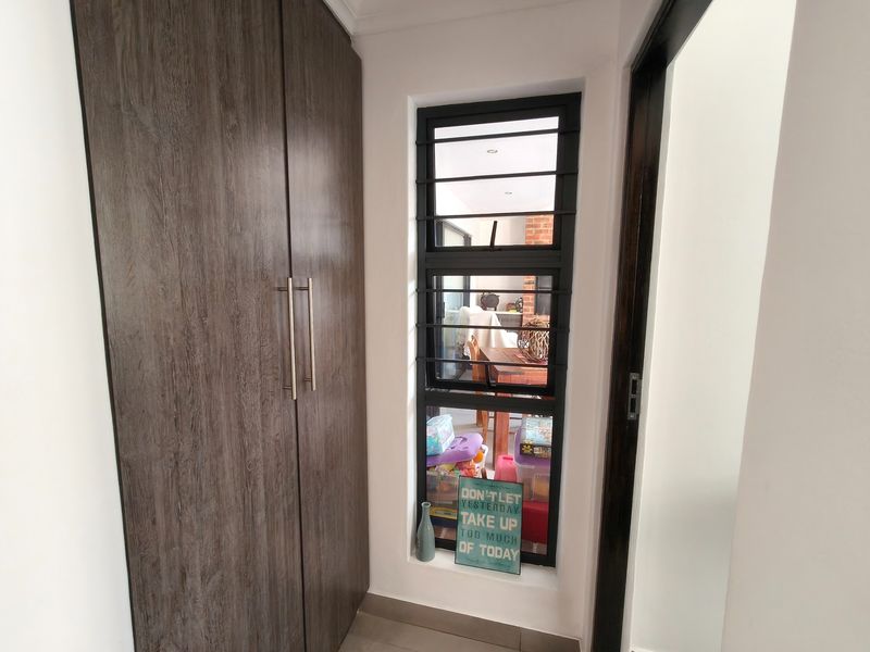 A clean hallway featuring a tall, dark wood-grain built-in cupboard and a window fitted with security bars.