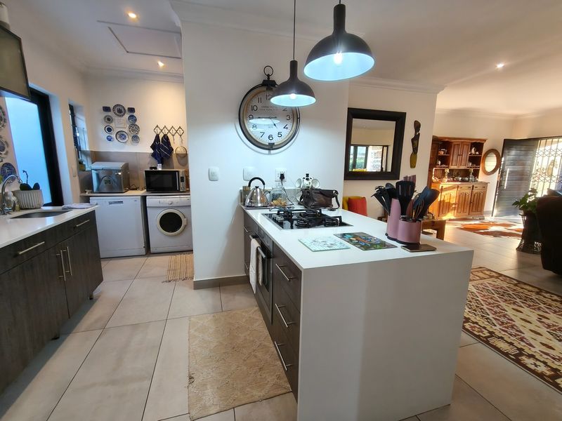 Modern open-plan kitchen featuring a central island with gas hob, stone countertops, sleek cabinetry, and contemporary pendant lighting, seamlessly flowing into the living area.