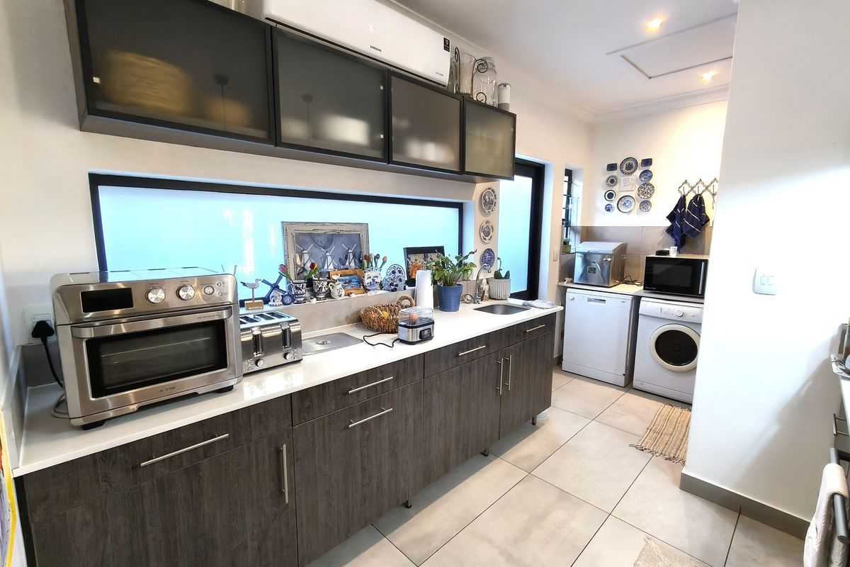 Modern kitchen featuring dark wood-grain cabinetry, stone countertops, stainless steel sink, and wall-mounted air conditioning unit with neutral tiled flooring.