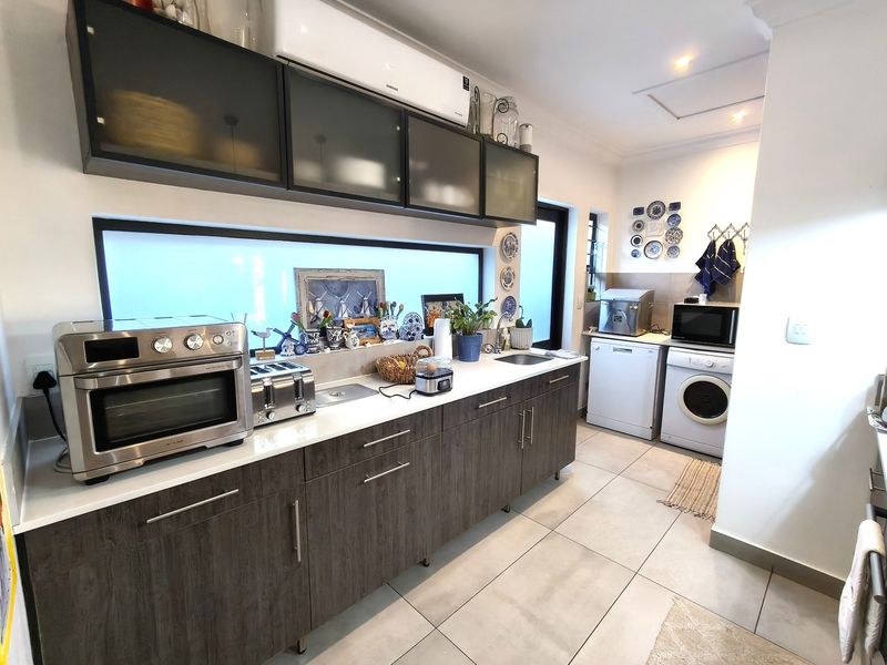 Modern kitchen featuring dark wood-grain cabinetry, stone countertops, stainless steel sink, and wall-mounted air conditioning unit with neutral tiled flooring.