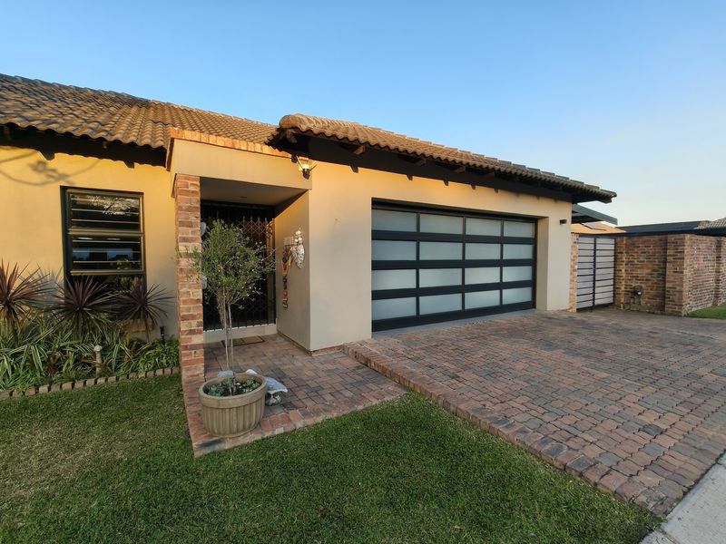 Front elevation of a modern home featuring a brick paved driveway, a contemporary frosted glass sectional garage door, and a covered entrance with security gate.
