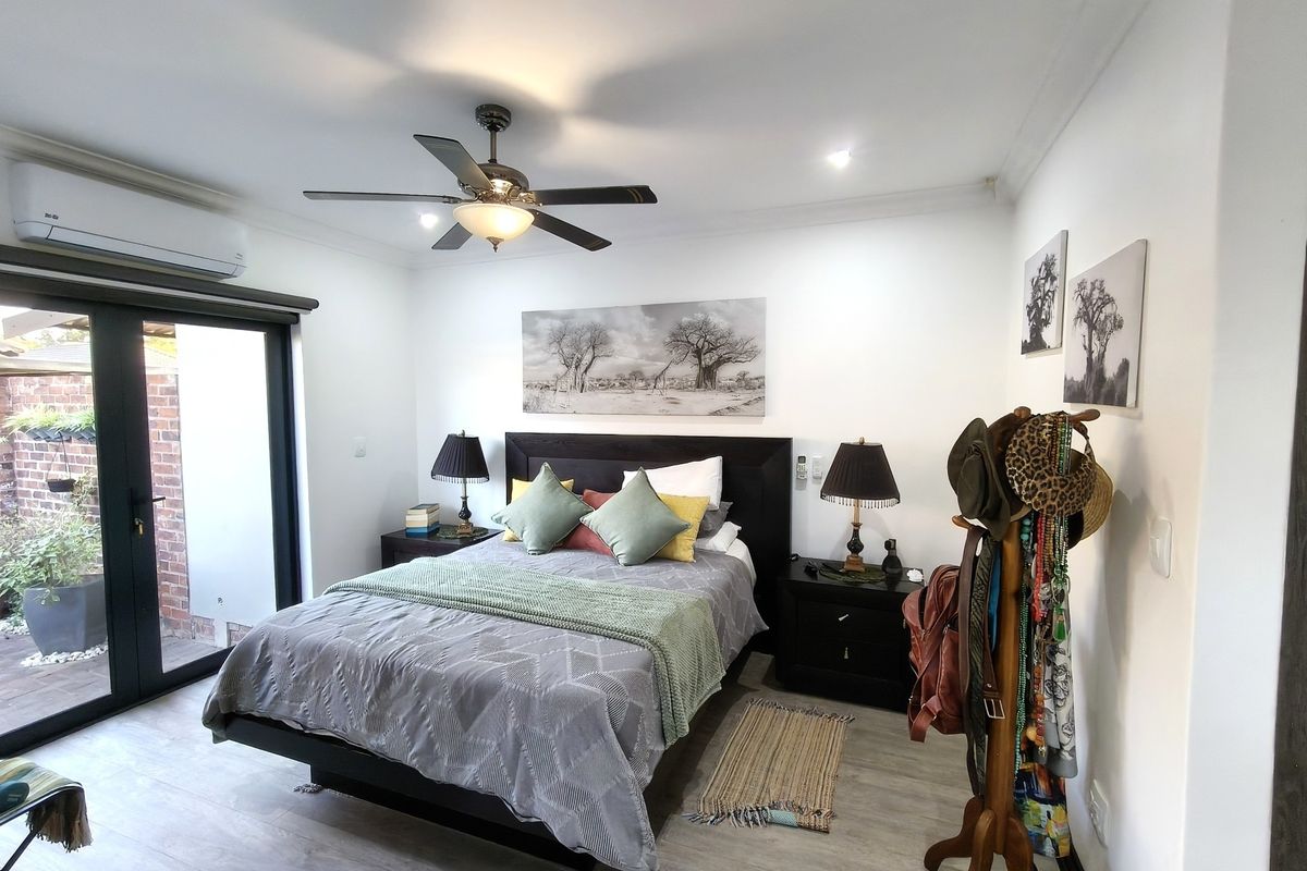A well-maintained bedroom featuring laminate flooring, a ceiling fan, split-system air conditioning, and direct access to an outdoor area through sliding glass doors.
