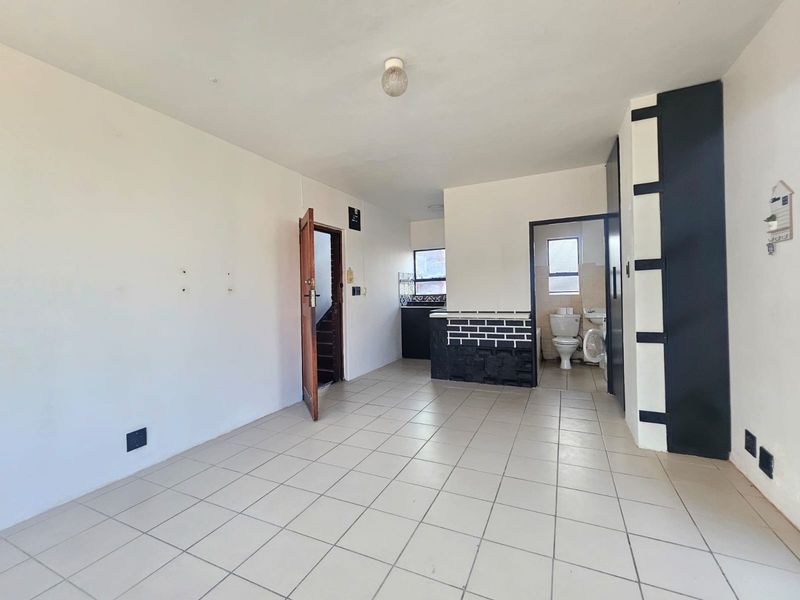 An open-plan living area featuring tiled flooring, a small kitchen counter, and an adjacent bathroom with a toilet and washbasin.
