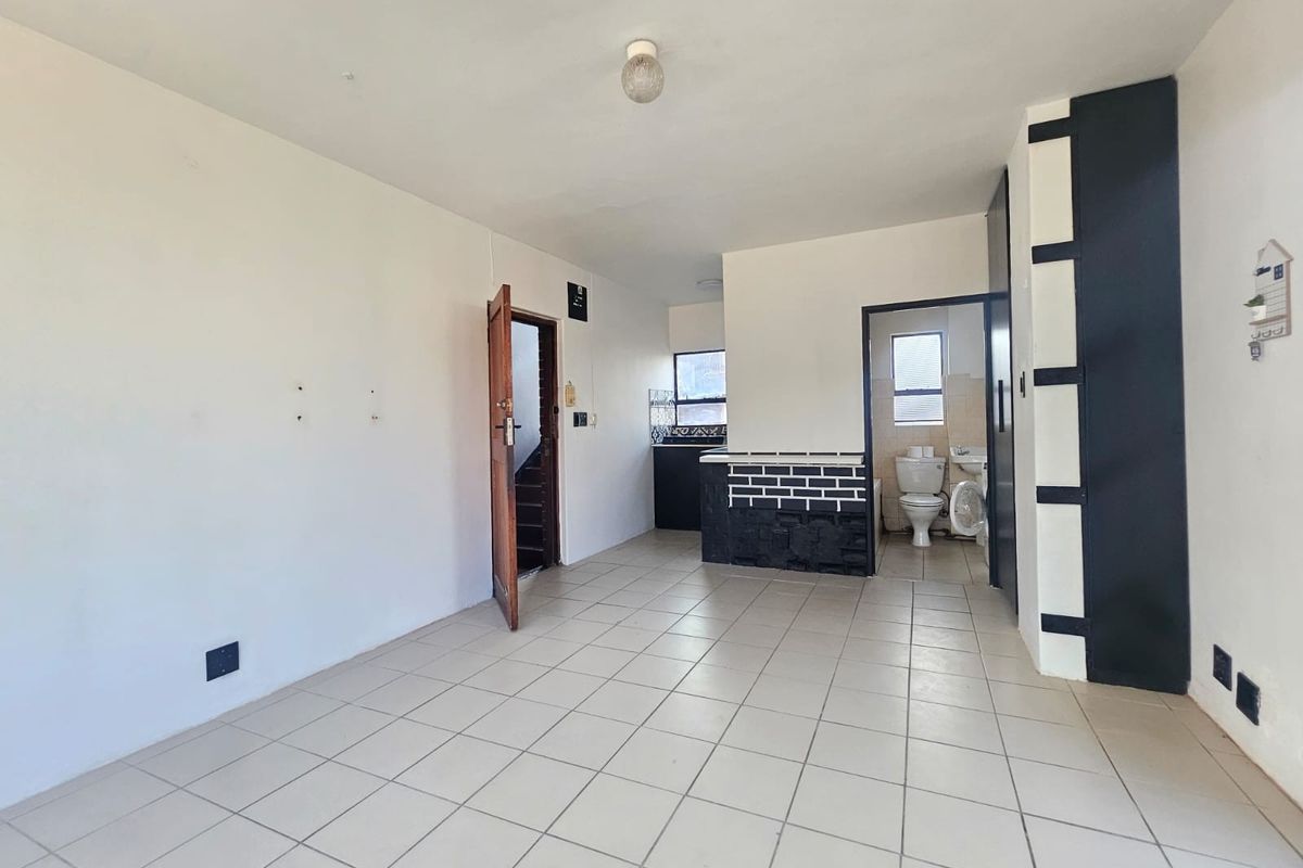 An open-plan living area featuring tiled flooring, a small kitchen counter, and an adjacent bathroom with a toilet and washbasin.