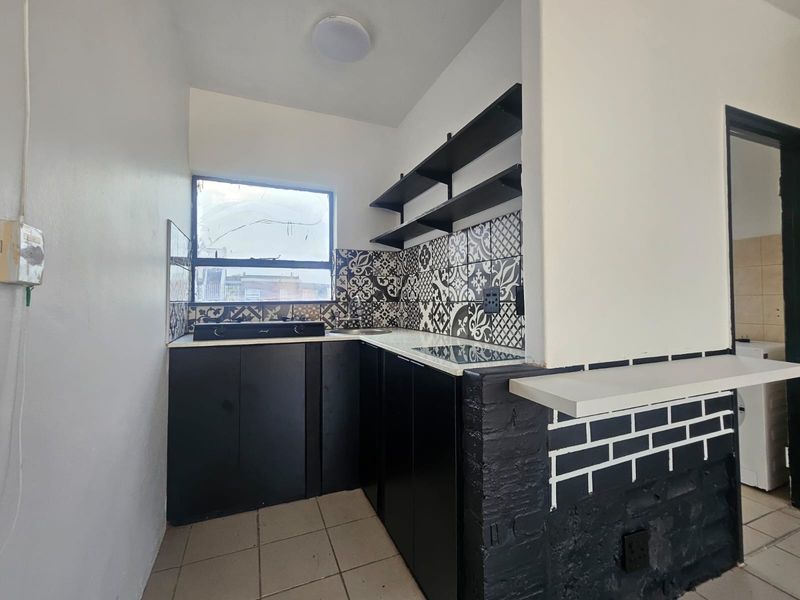 Compact kitchen featuring black cabinetry, patterned tiled backsplash, open shelving, and a breakfast counter, providing a functional and modern aesthetic.
