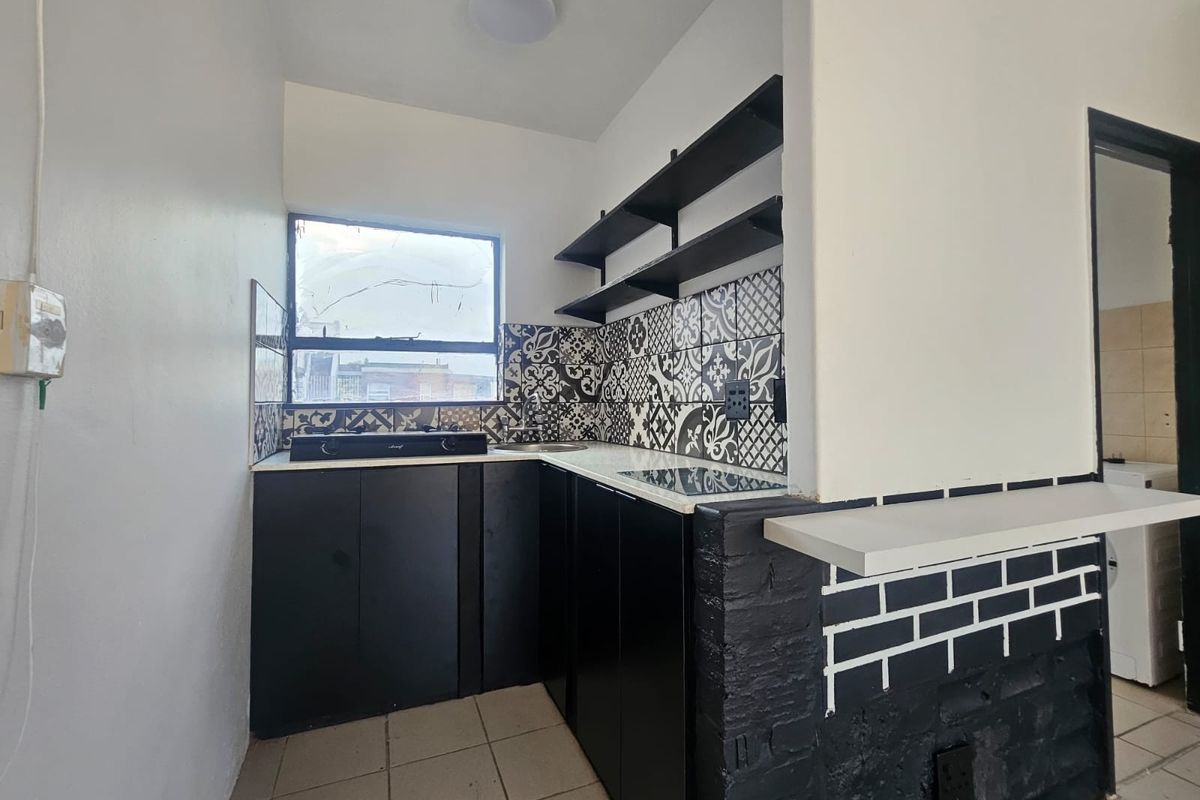 Compact kitchen featuring black cabinetry, patterned tiled backsplash, open shelving, and a breakfast counter, providing a functional and modern aesthetic.