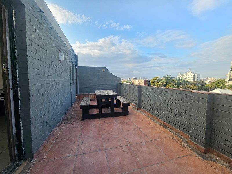 Spacious rooftop balcony featuring painted brick walls, tiled flooring, and an open-air setting with urban views.