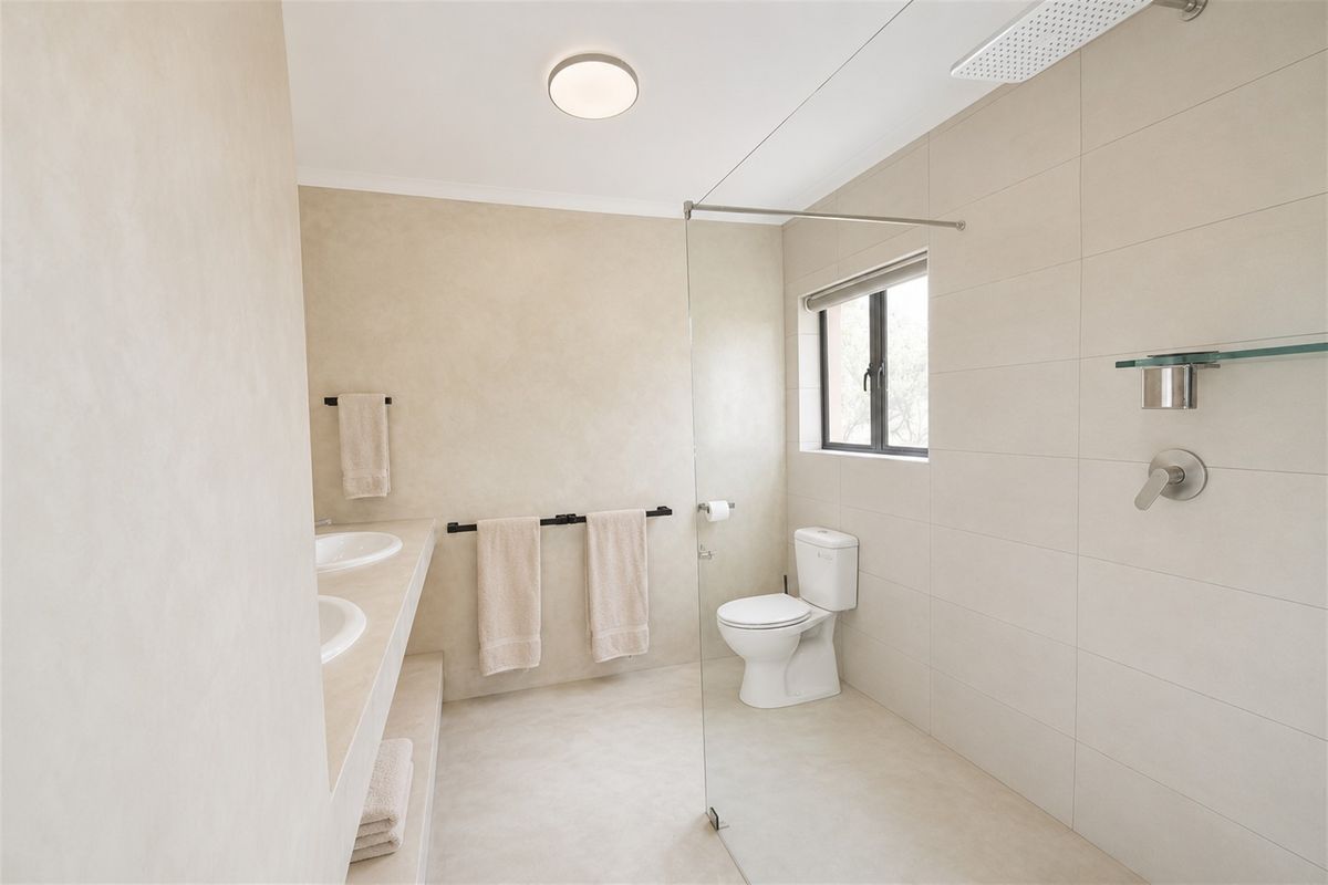 Modern bathroom featuring a double vanity, walk-in shower with glass screen, rain shower head, and neutral tiled finishes throughout.
