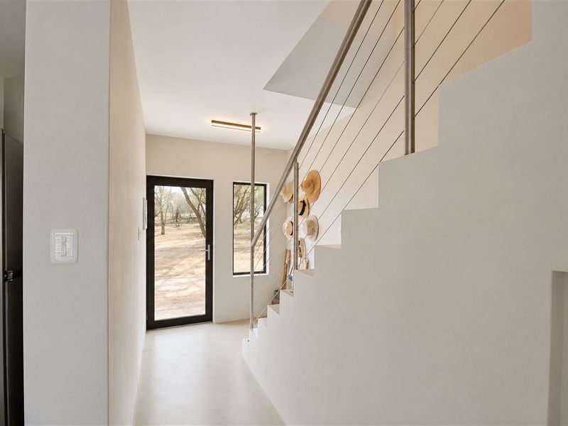 Bright and modern entrance hall featuring a clean staircase with a stainless steel balustrade and direct access to the exterior.