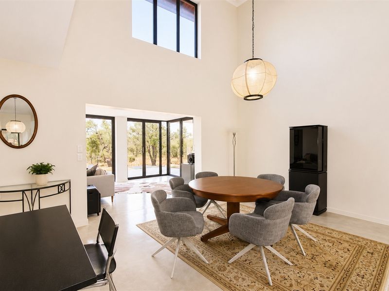 Spacious open-plan dining area featuring double-volume ceilings, polished concrete floors, and large sliding doors that provide seamless access to the outdoor area.