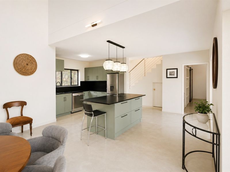 Modern open-plan kitchen featuring sage green cabinetry, a central island with dark countertops, and a staircase leading to the upper level.